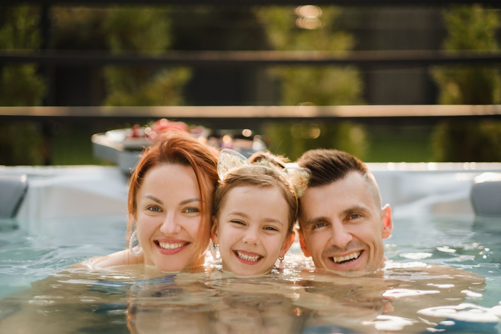 A joyful family enjoying a relaxing evening in a backyard hot tub, surrounded by lush greenery and warm sunlight.