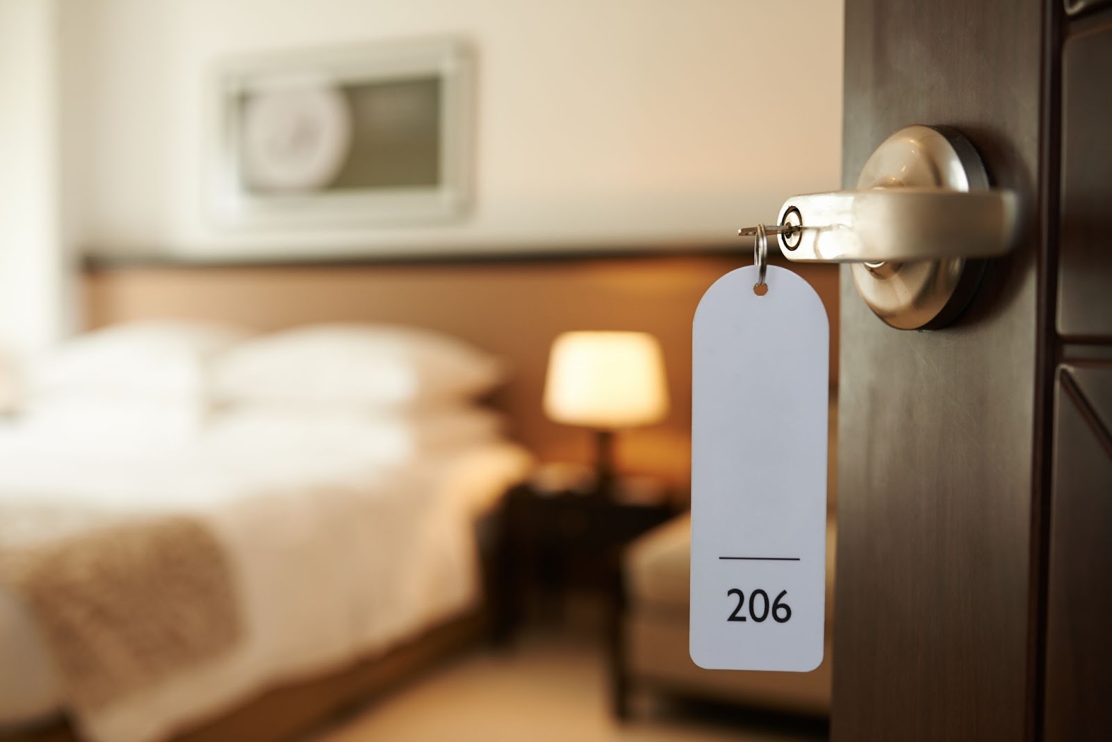 Hotel room door with a "206" tag, showing a bed and lamp inside.