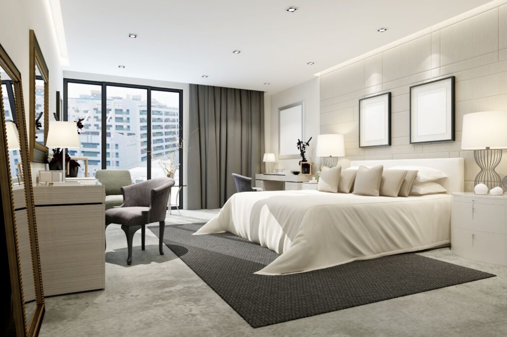 Modern bedroom with a large bed, chairs, and city view through large windows.