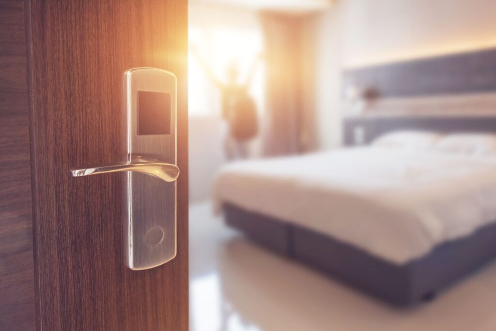 Open hotel room door with keycard lock and bed in soft focus.