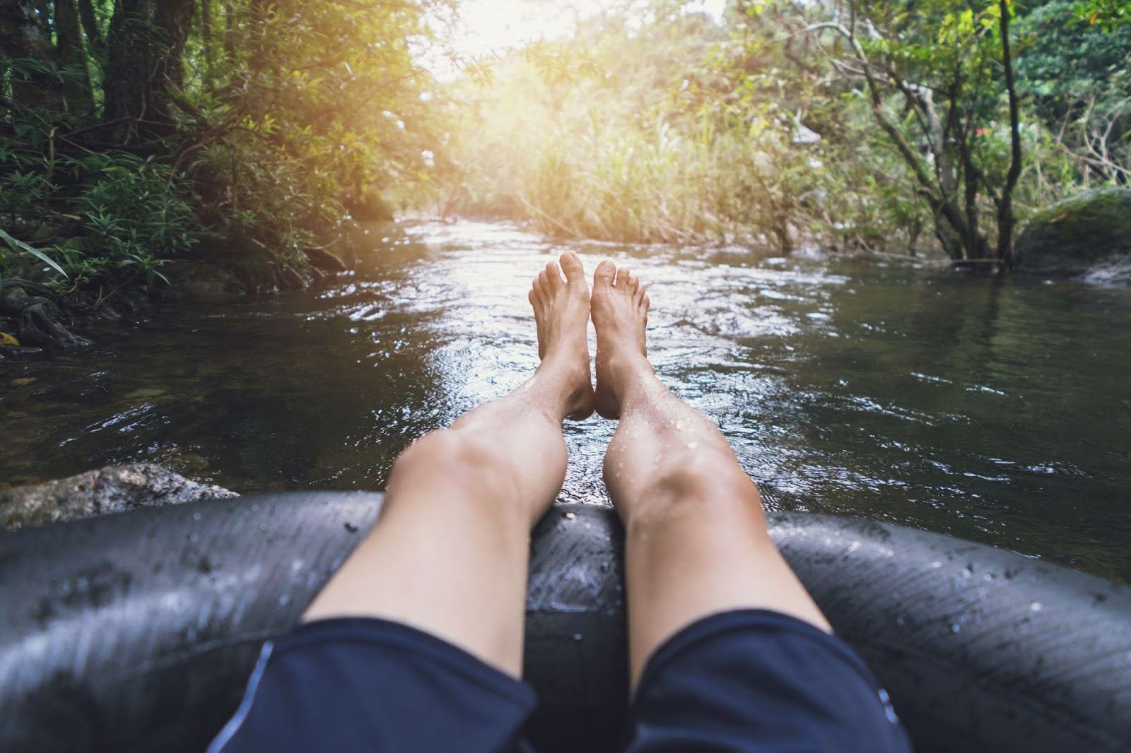 Feet of a person relaxing on an inner tube gently drifting in a river surrounded by greenery