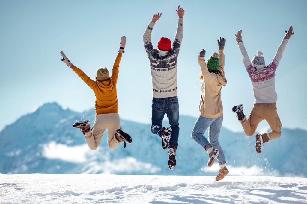 Four people joyfully jumping in the air on a snowy mountain surrounded by a pristine winter landscape