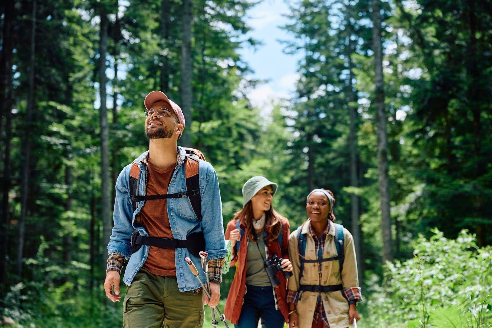 Three people with backpacks walking together on a trail through a dense green forest