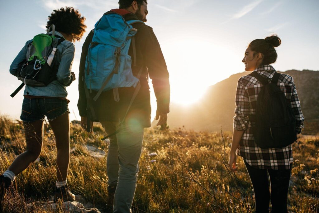 Three hikers with backpacks walking along a mountain trail surrounded by rocky terrain and distant peaks