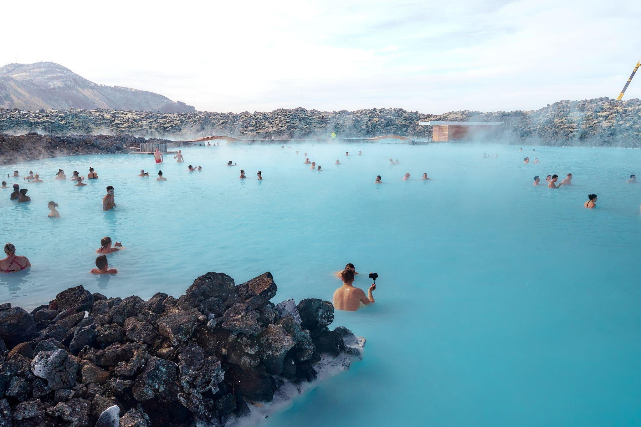 A group enjoys swimming in the clear blue waters of the Blue Lagoon against a scenic backdrop