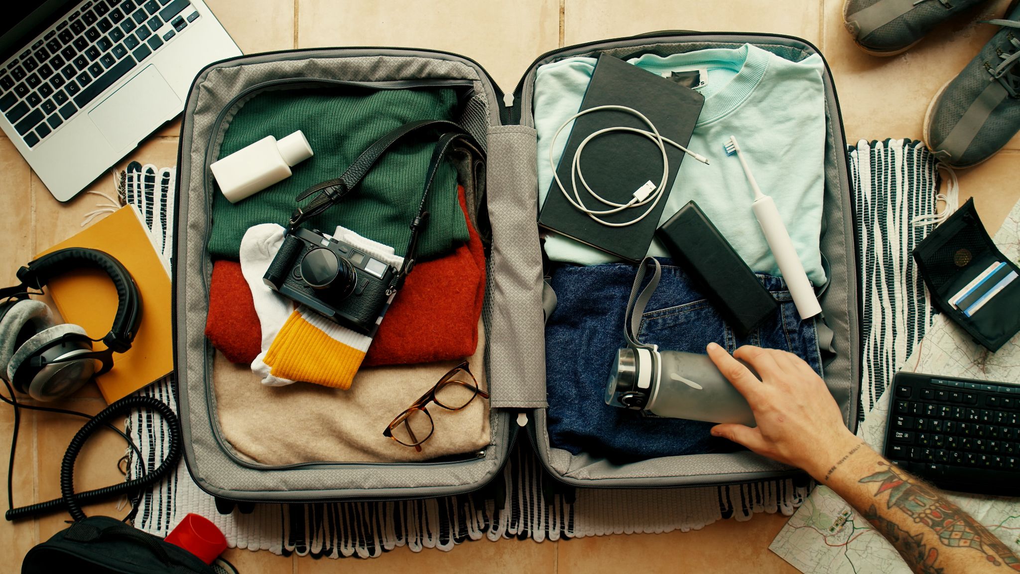 Top-down view of an open suitcase neatly packed with clothes, electronics, camera, and travel essentials.