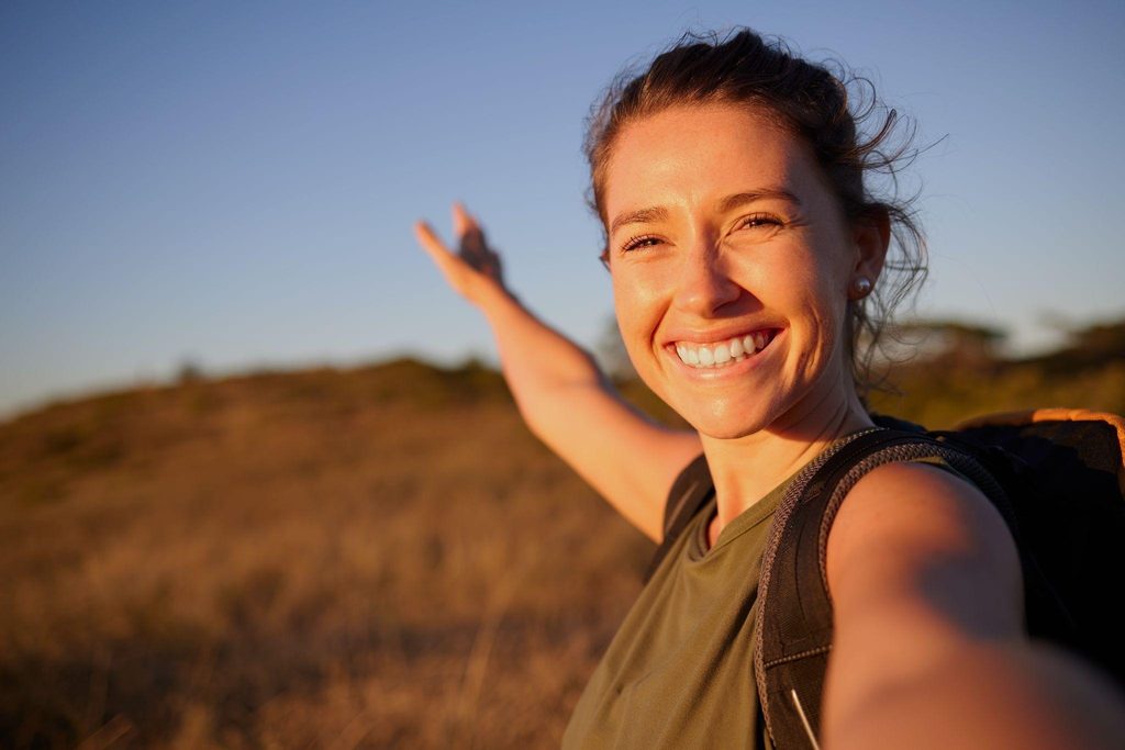 A woman stands in a field with her arms outstretched embracing the open space and nature around her